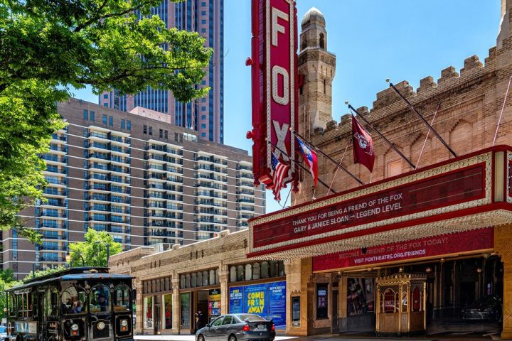 a double decker bus driving down a street next to tall buildings with Fox Theatre in the background