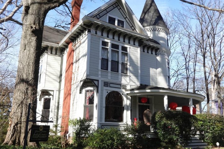Victorian-style house with turret, porch, red brick chimney, and winter trees surrounding it.