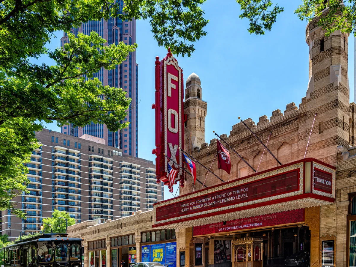 a double decker bus driving down a street next to tall buildings with Fox Theatre in the background