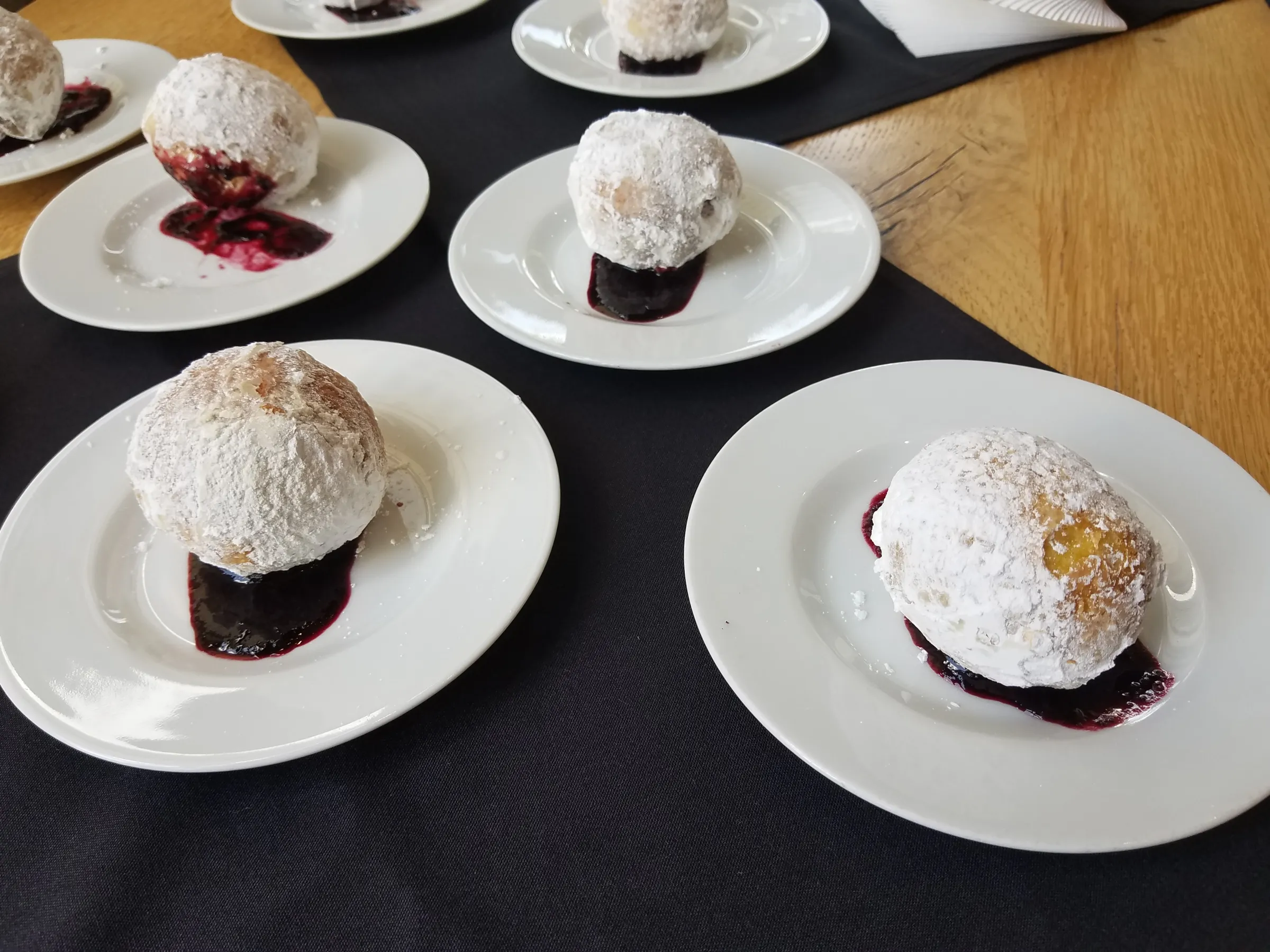 Powdered doughnuts on plates with berry sauce.