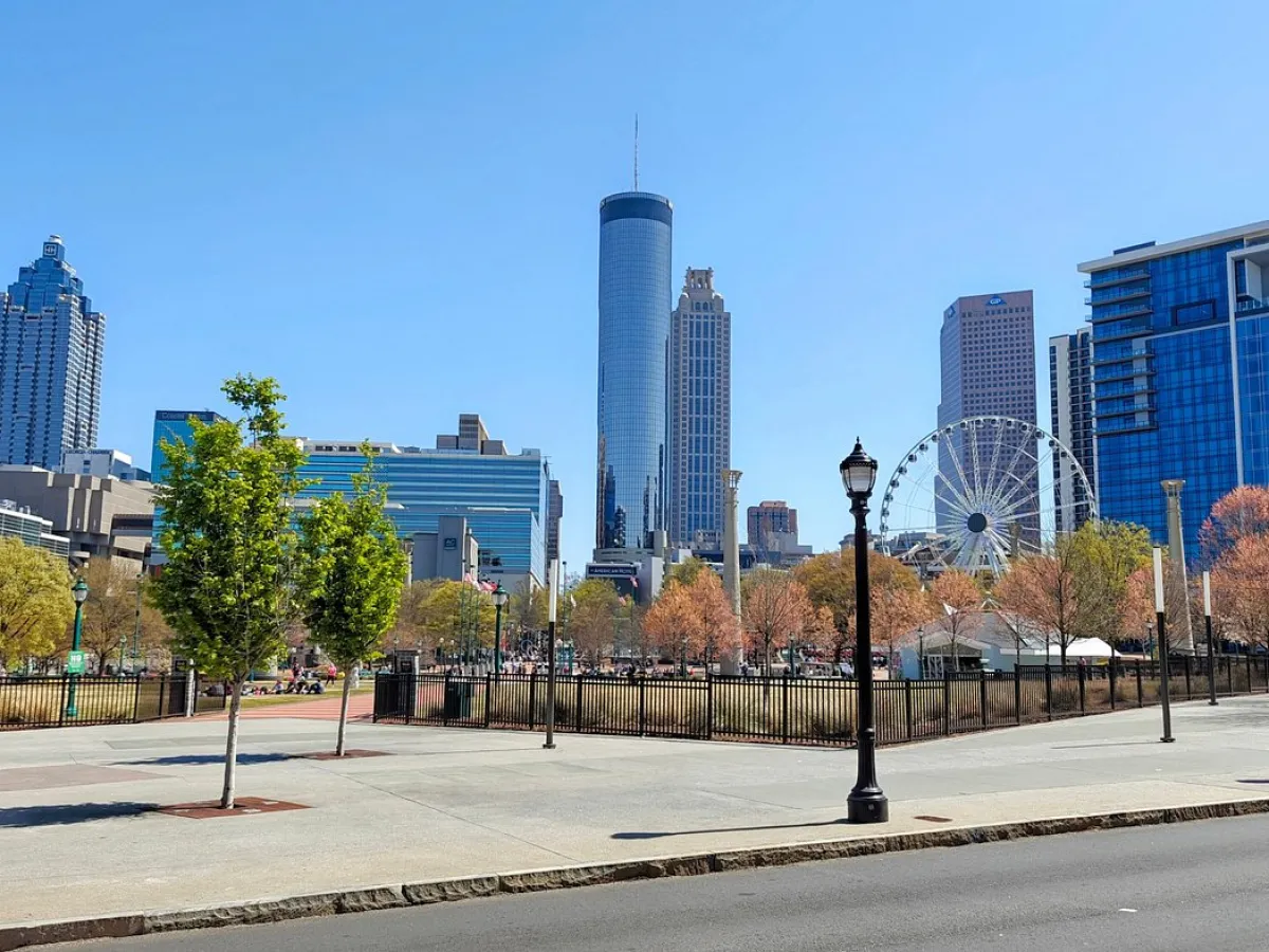Cityscape with tall buildings, Ferris wheel, trees, and street lamps on a sunny day.