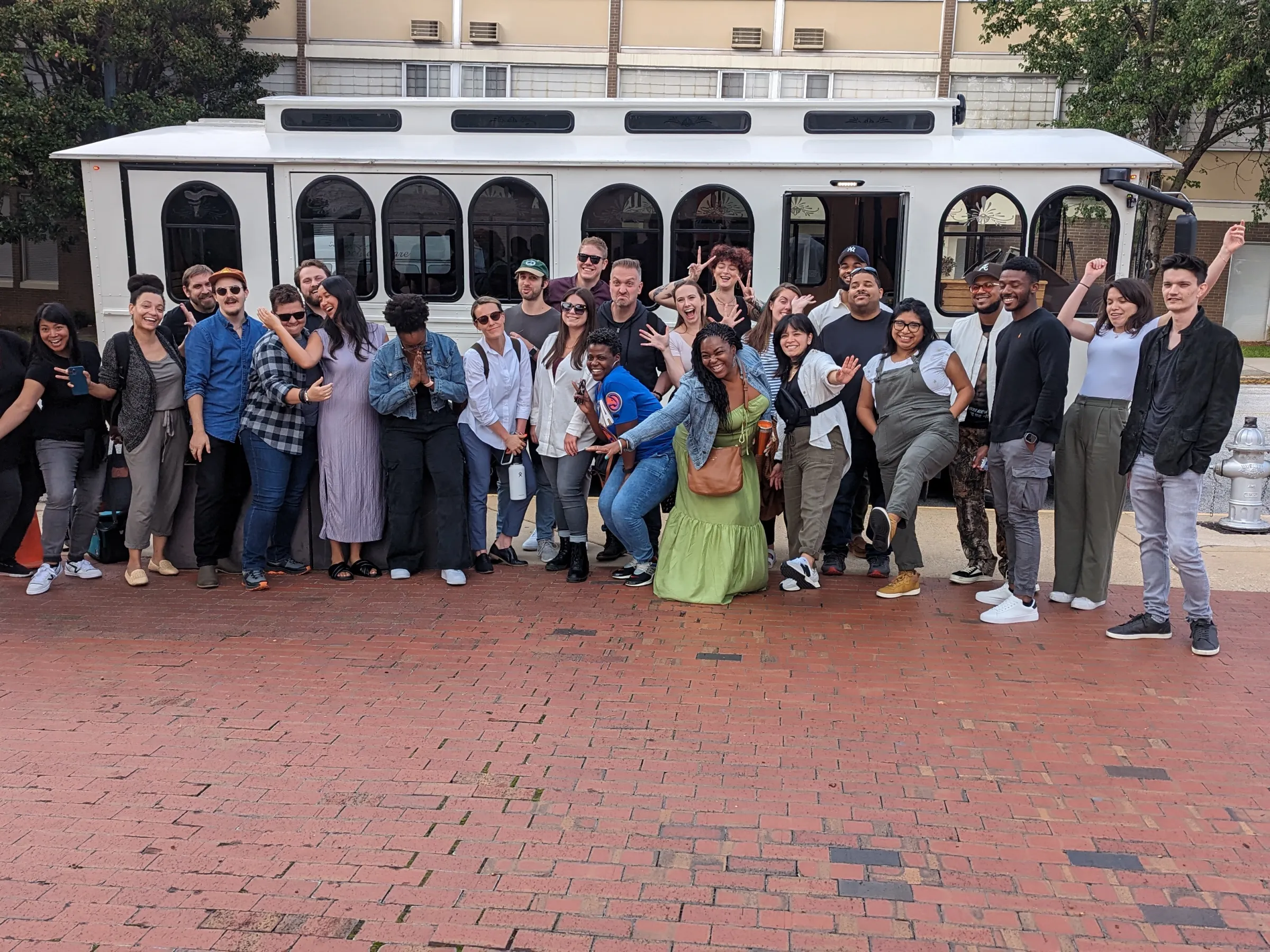 Group of people posing enthusiastically in front of a white trolley on a city street.