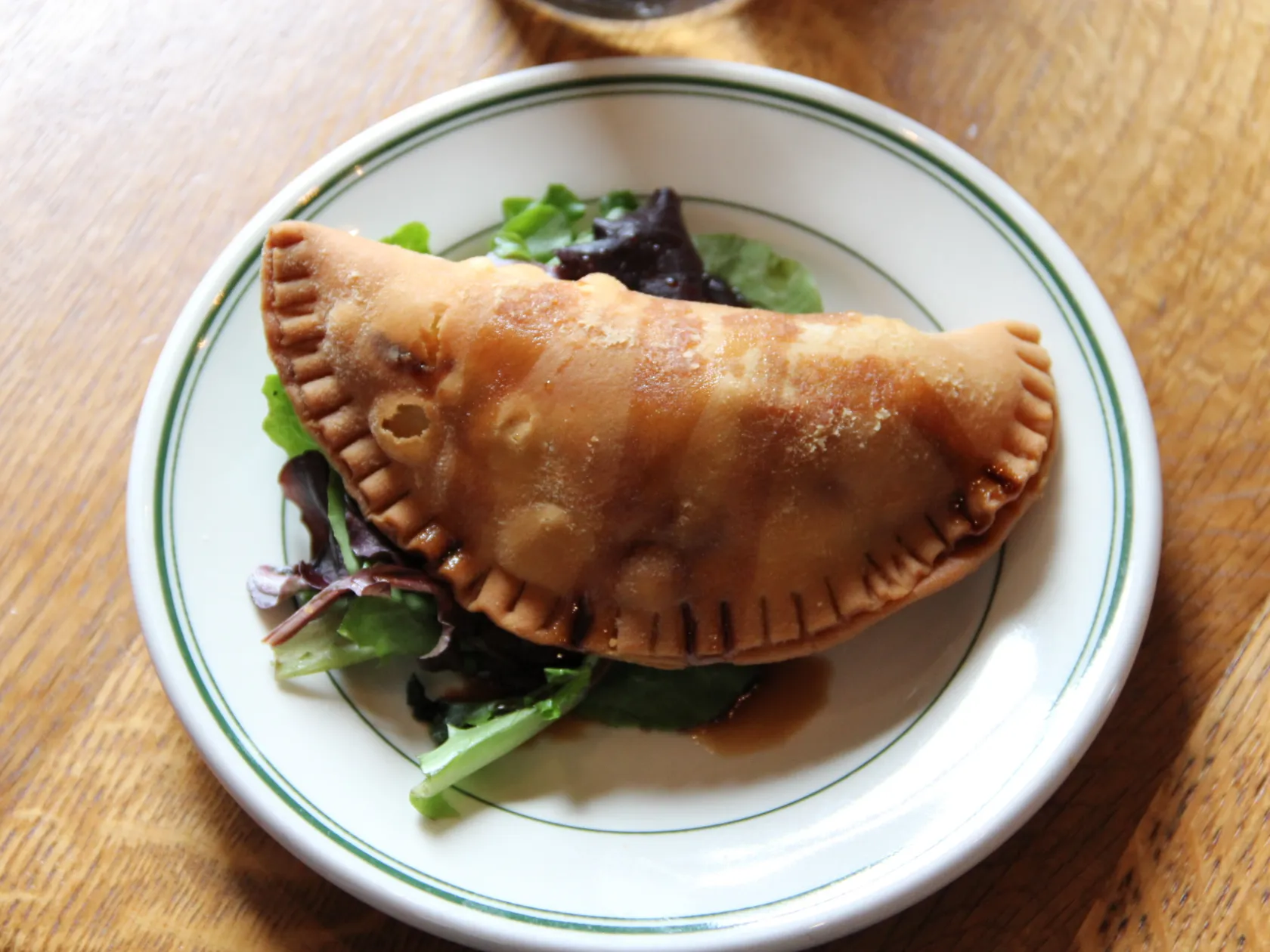 A fried empanada on a bed of greens on a white plate.