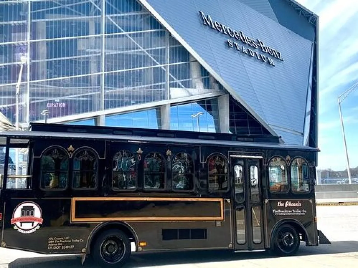 Black trolley in front of a large stadium with angular design on a sunny day.