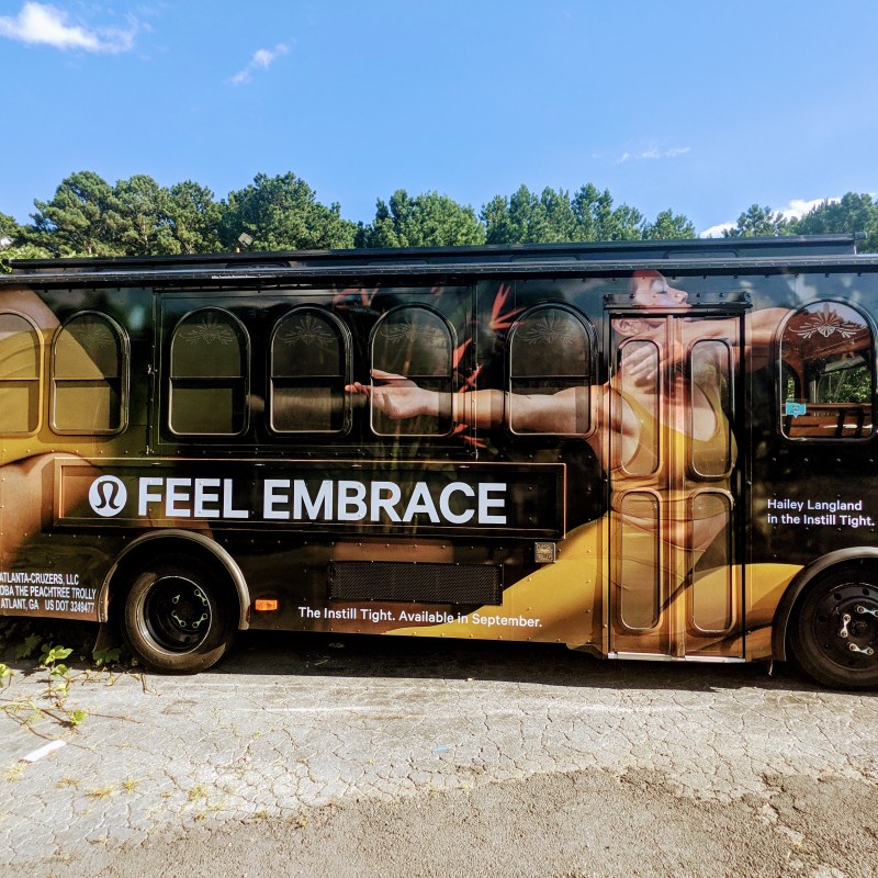 Trolley bus with Lululemon ad featuring 'FEEL EMBRACE' and an athlete stretching in yellow attire.