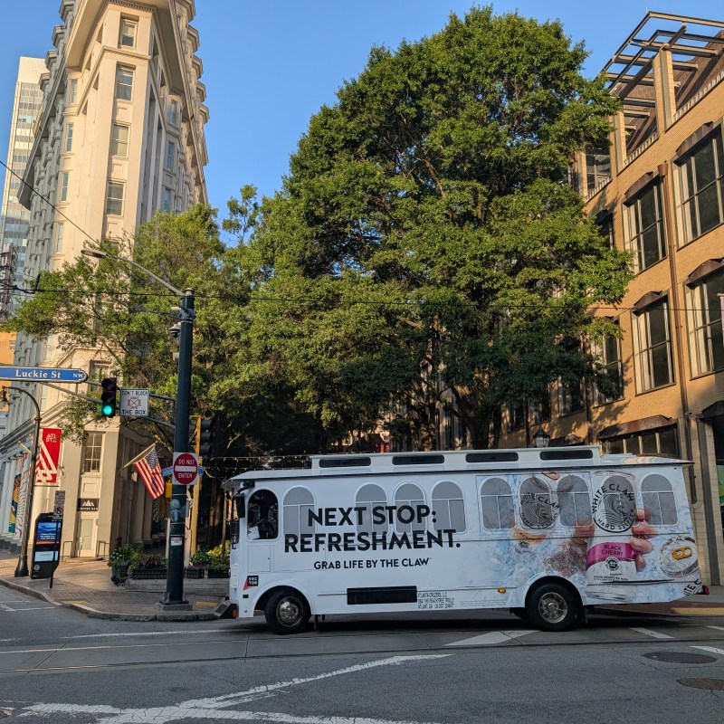 City street with a trolley featuring a beverage advertisement and buildings in the background.