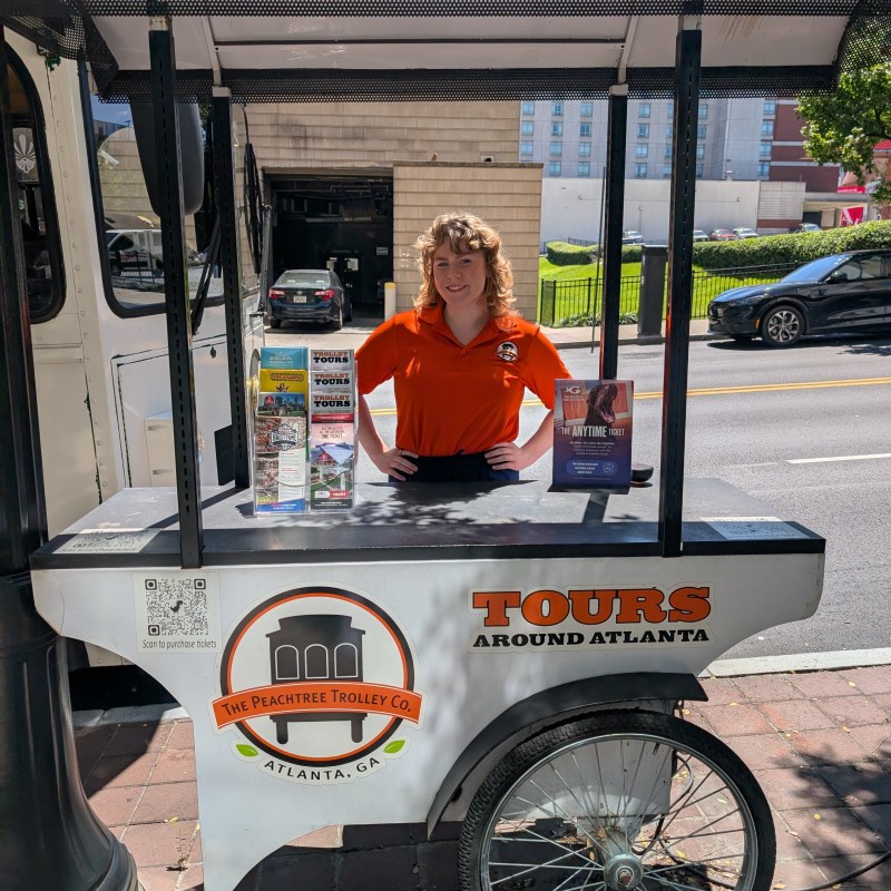 Person in orange shirt at trolley tour booth in Atlanta, GA, with brochures on display.