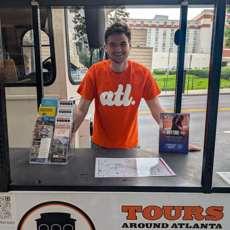 Person in orange shirt stands at tour booth with brochures in Atlanta.