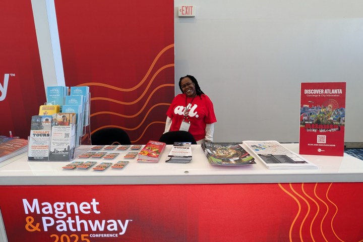 Booth with 'Discover Atlanta' sign, brochures, and a smiling person in a red shirt at a conference.