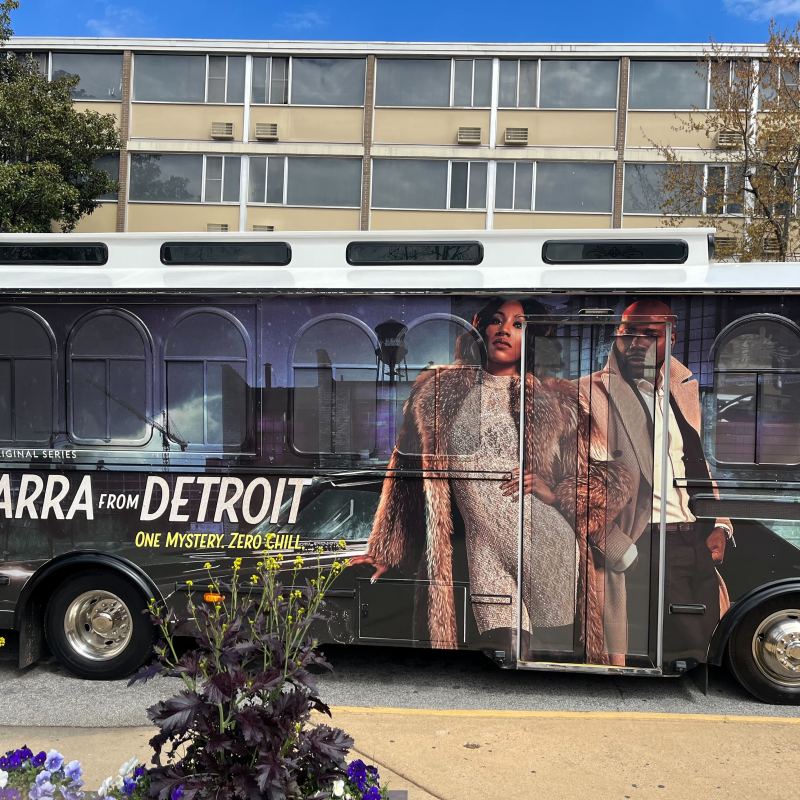 Bus with 'Diarra from Detroit' series ad parked on street.