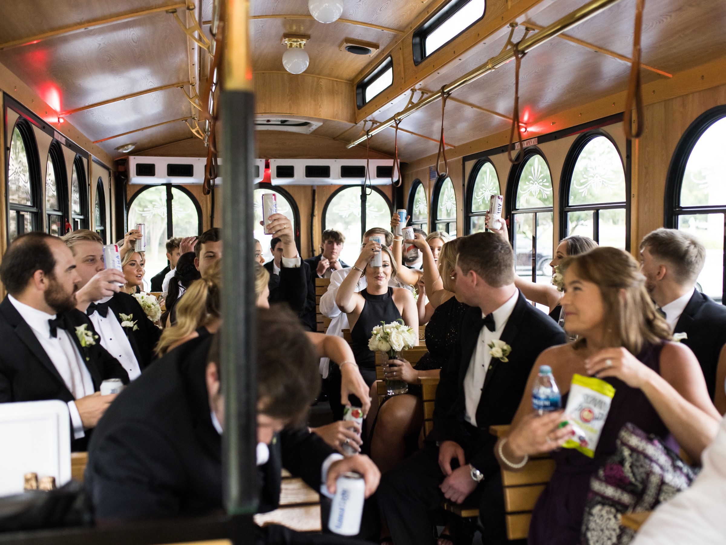 People in formal attire celebrate with drinks inside a trolley bus.