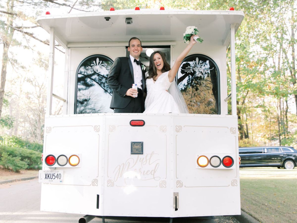 Bride and groom in wedding attire standing on the back of a 'Just Married' trolley.
