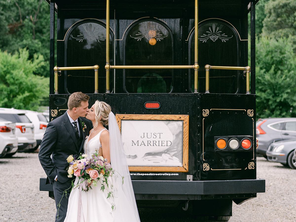 Bride and groom kiss in front of a trolley with 'Just Married' sign.