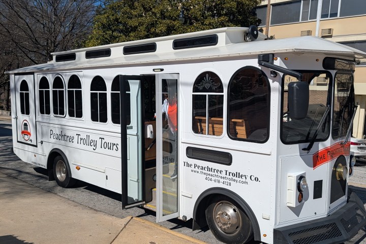 White Peachtree trolley parked on street, doors open, with trees and building in background.